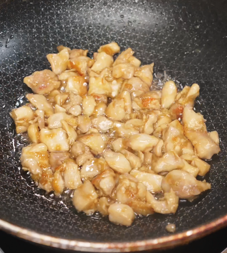 Small diced chicken pieces sizzle in a pan with a light coating of oil, turning golden as they cook. This is the first step in preparing kung pao chicken, ensuring the meat is seared and juicy before the vegetables and sauce are added.