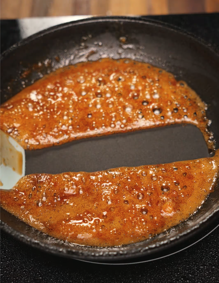A close-up shot of honey garlic sauce simmering in a nonstick skillet, with visible bubbling and caramelization. This golden, sticky glaze is made from garlic, soy sauce, and honey, and will later be brushed over tender chicken thighs. Perfect for weeknight dinners or meal prep, this sauce adds a sweet and savory punch to any Asian-inspired chicken recipe.