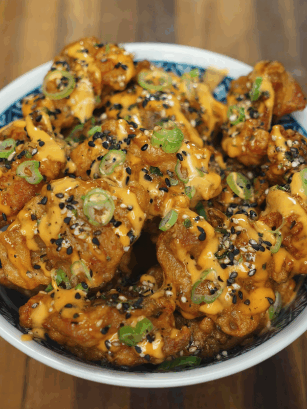 Final presentation of mochiko chicken topped with spicy mayo, sliced green onions, and black sesame seeds in a decorative bowl.