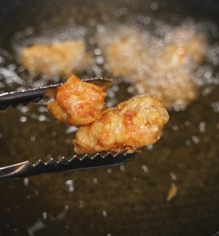Close-up of crispy golden brown fried chicken being lifted from hot oil with tongs during frying process.