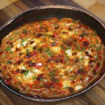 The completed peanut chili oil shakshuka served in the skillet, topped with drizzles of sauce, crispy chili oil, and finely chopped herbs.