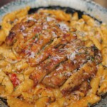 A bowl of penne pasta smothered in creamy tomato sauce is topped with sliced seared chicken and freshly grated parmesan in the Marry Me Chicken pasta dish.