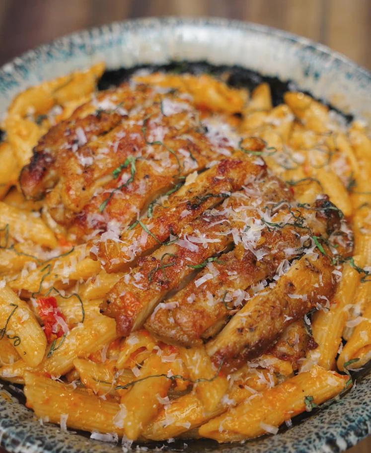 A bowl of penne pasta smothered in creamy tomato sauce is topped with sliced seared chicken and freshly grated parmesan in the Marry Me Chicken pasta dish.