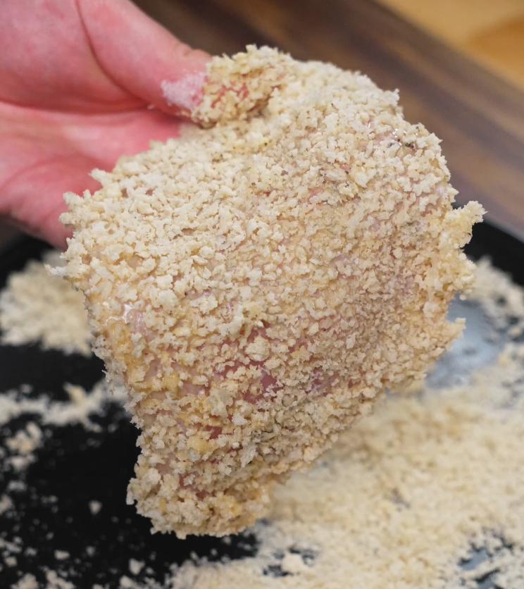 A raw pork cutlet coated in panko breadcrumbs, held up and ready to be fried for the katsudon.