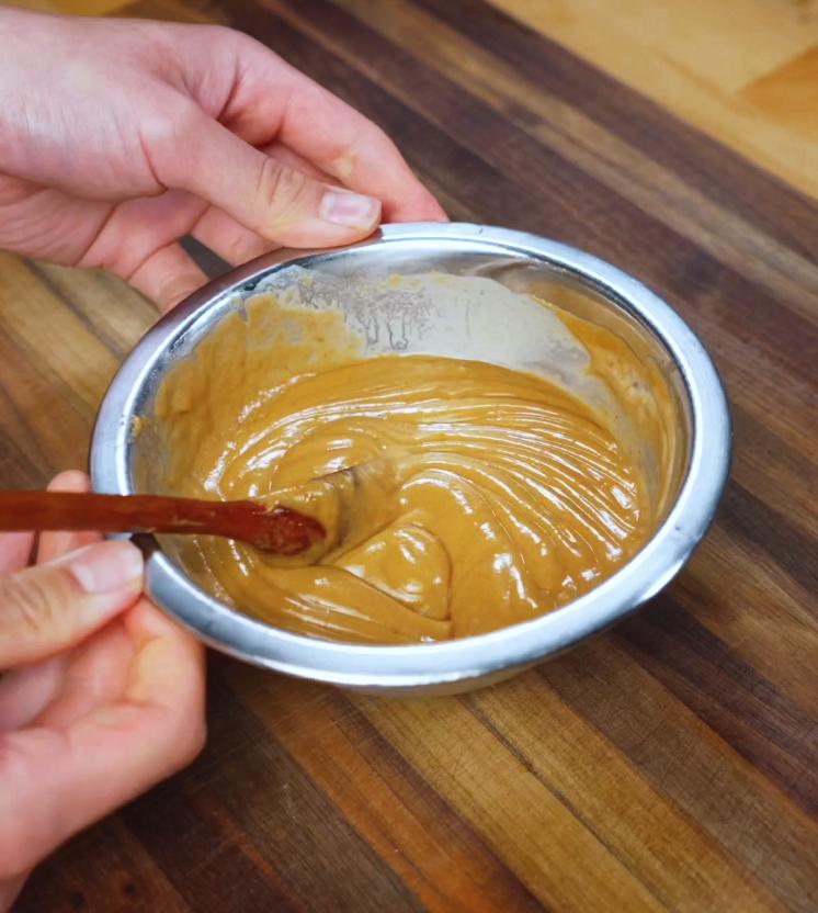 A thick and creamy peanut butter sauce being stirred in a metal bowl, creating a smooth and nutty element for the spicy shakshuka recipe.
