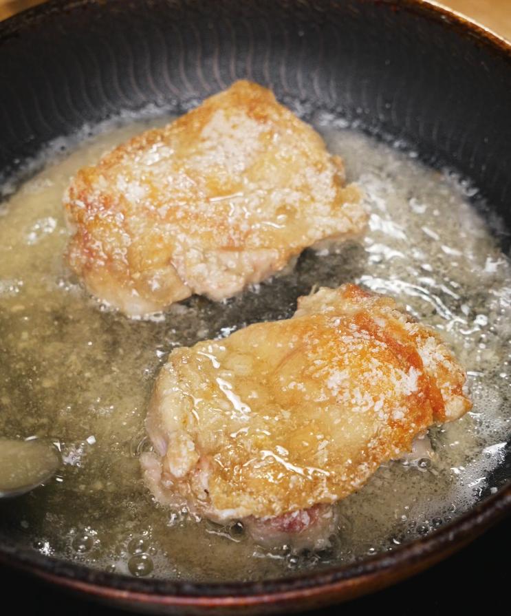 Chicken thighs sizzling in hot oil in a nonstick skillet, developing a golden crispy crust as the first step in the honey lemon chicken cooking process.