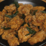Finished Taiwanese popcorn chicken served in a black bowl, golden brown and flecked with fried basil leaves.