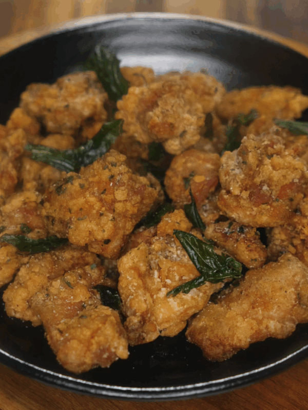 Finished Taiwanese popcorn chicken served in a black bowl, golden brown and flecked with fried basil leaves.
