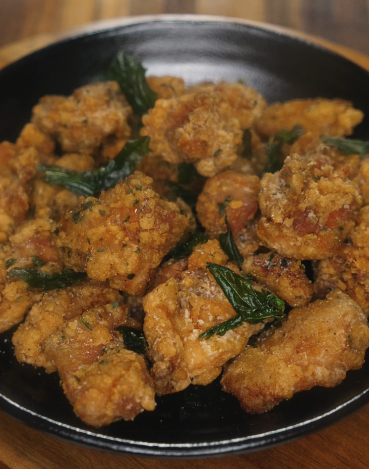 Finished Taiwanese popcorn chicken served in a black bowl, golden brown and flecked with fried basil leaves.