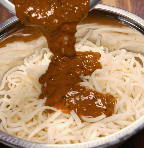 Spicy dan dan sauce being poured over cooked noodles in a metal bowl — ready to toss and serve.