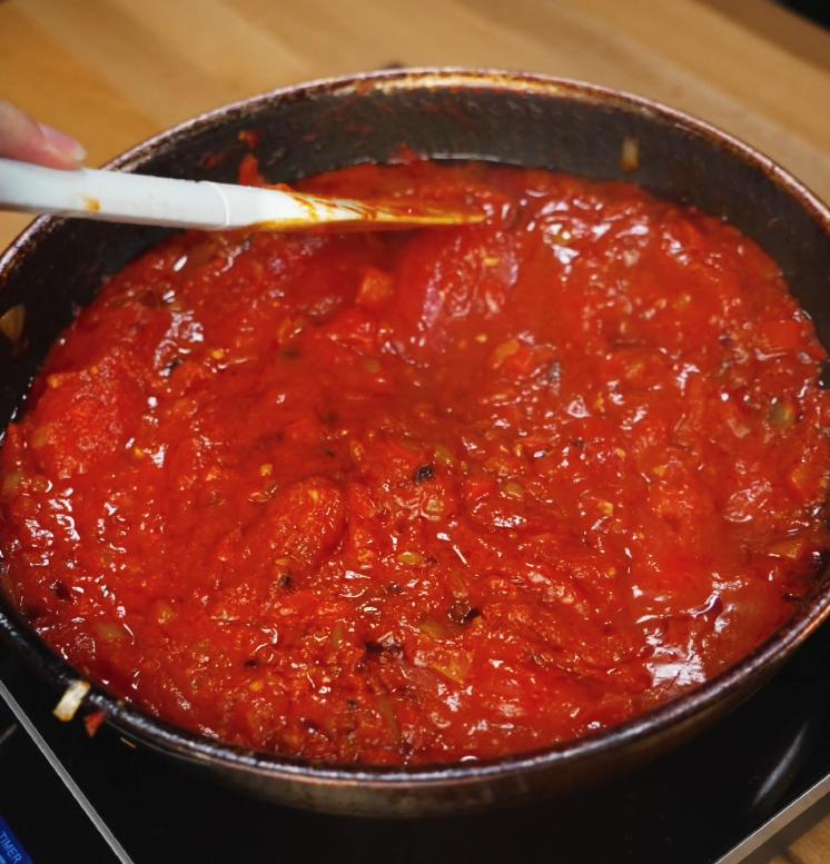 The tomato and chili sauce gently bubbling in a skillet as it reduces into a thick, savory base for the peanut chili oil shakshuka.