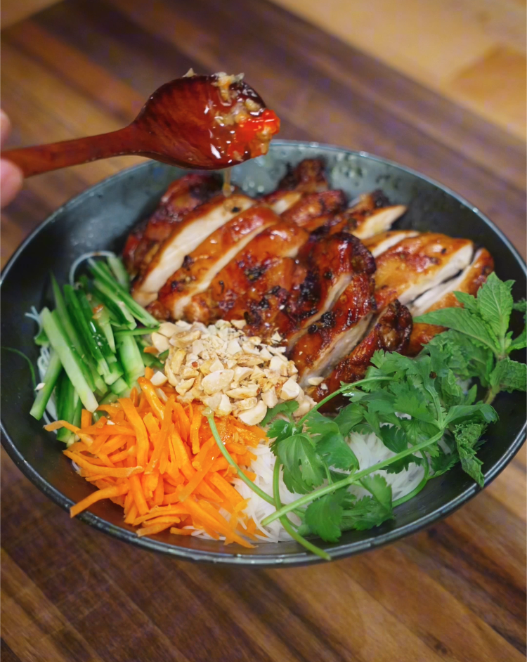 A spoonful of homemade nuoc cham dipping sauce being drizzled over a bowl of Vietnamese grilled chicken and vermicelli noodles.