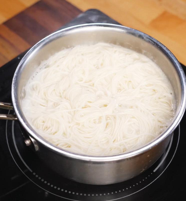 A pot filled with boiling somen noodles on the stovetop, just about to be drained and chilled for the base of the refreshing somen salad.