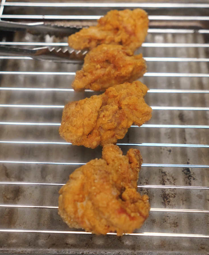 Freshly fried chicken drumettes resting on a wire rack, golden brown and crispy.