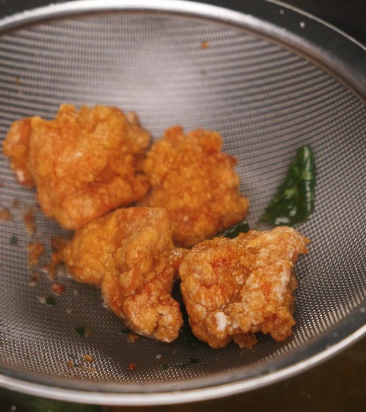 Golden brown chicken pieces frying in oil, developing a crunchy exterior while basil leaves float alongside.