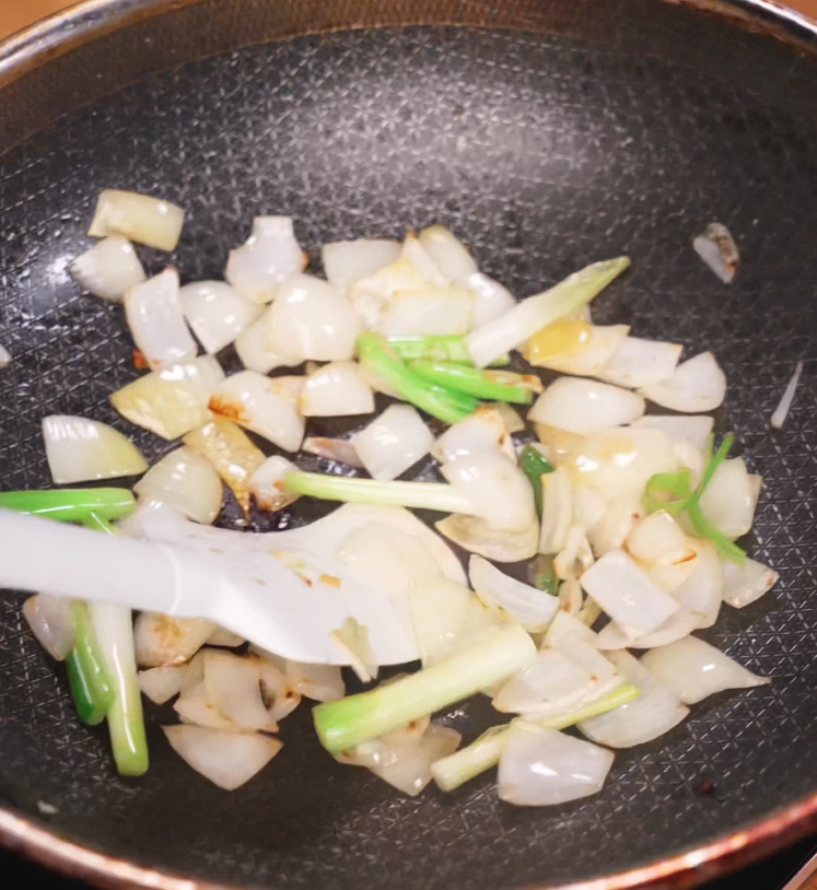 Frying chopped white onions and scallions in a pan until lightly browned and softened, adding aromatic base to the stir fry.