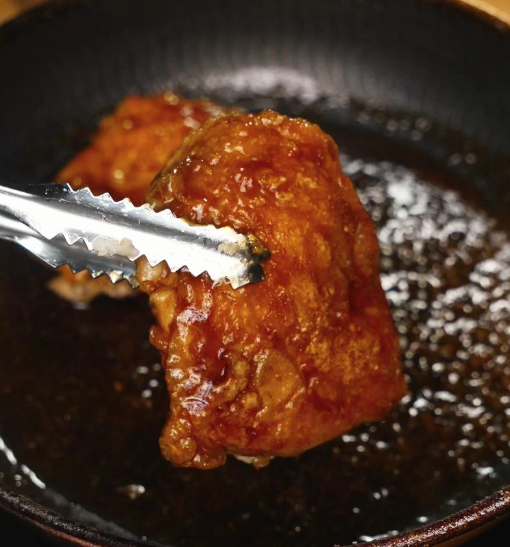 Crispy chicken thigh being coated in the sticky, glossy honey lemon sauce while still in the pan to ensure maximum flavor absorption.