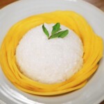 Final plated dish of mango sticky rice with sliced mango arranged in a ring and a sprig of mint on top for garnish.
