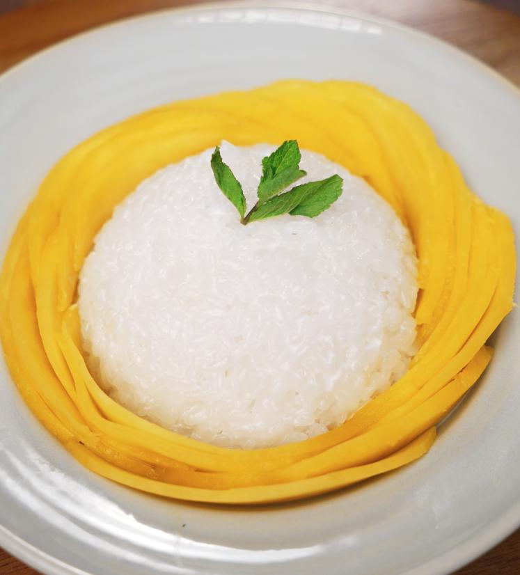 Final plated dish of mango sticky rice with sliced mango arranged in a ring and a sprig of mint on top for garnish.