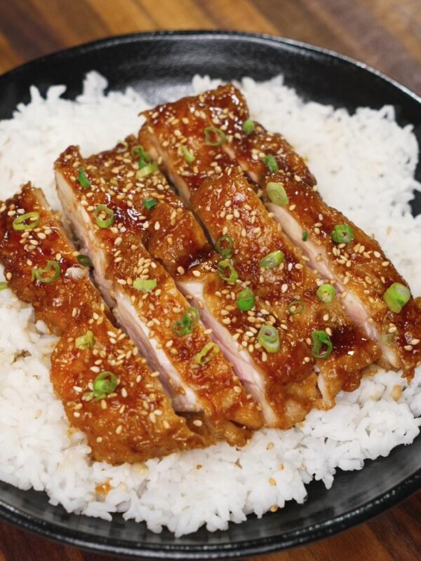 Final dish of honey lemon chicken sliced and served over a bed of fluffy white rice, garnished with sesame seeds and green onions for a perfect finish.