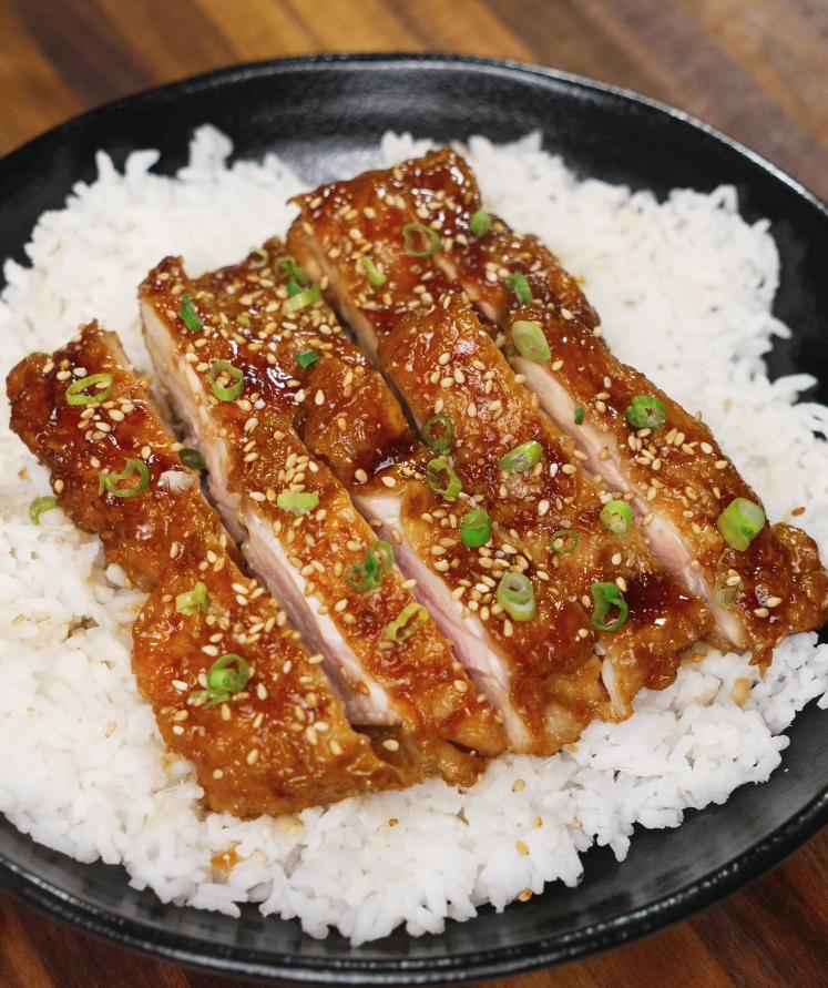 Final dish of honey lemon chicken sliced and served over a bed of fluffy white rice, garnished with sesame seeds and green onions for a perfect finish.