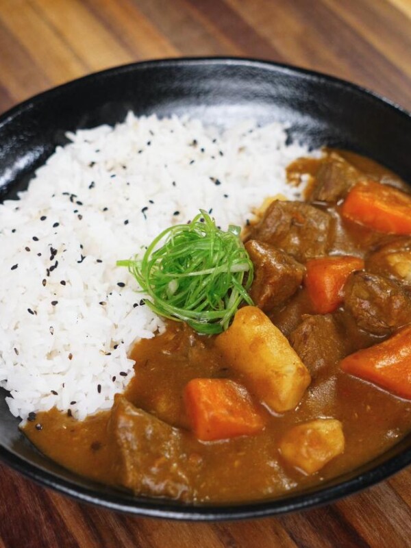A finished bowl of Japanese beef curry served with white rice, garnished with finely shredded scallions and black sesame seeds. The rich, glossy curry features chunks of beef, carrots, and potatoes.