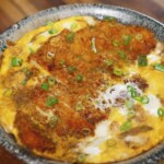 A bowl of freshly made katsudon featuring crispy pork cutlet simmered with egg and onions, garnished with chopped green onions.