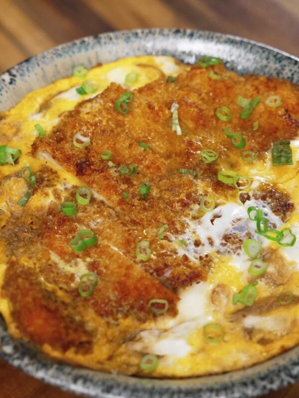 A bowl of freshly made katsudon featuring crispy pork cutlet simmered with egg and onions, garnished with chopped green onions.