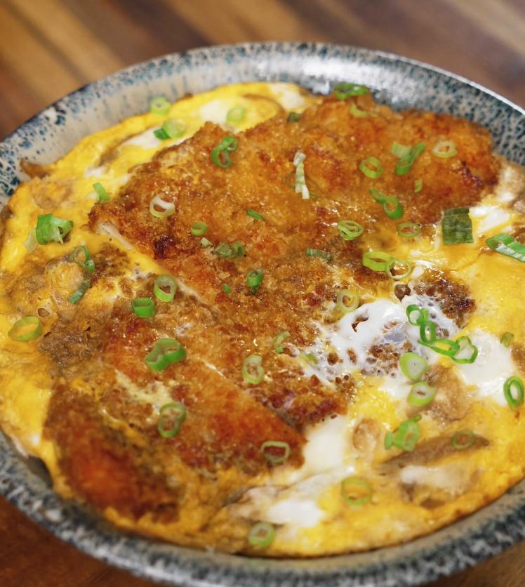 A bowl of freshly made katsudon featuring crispy pork cutlet simmered with egg and onions, garnished with chopped green onions.