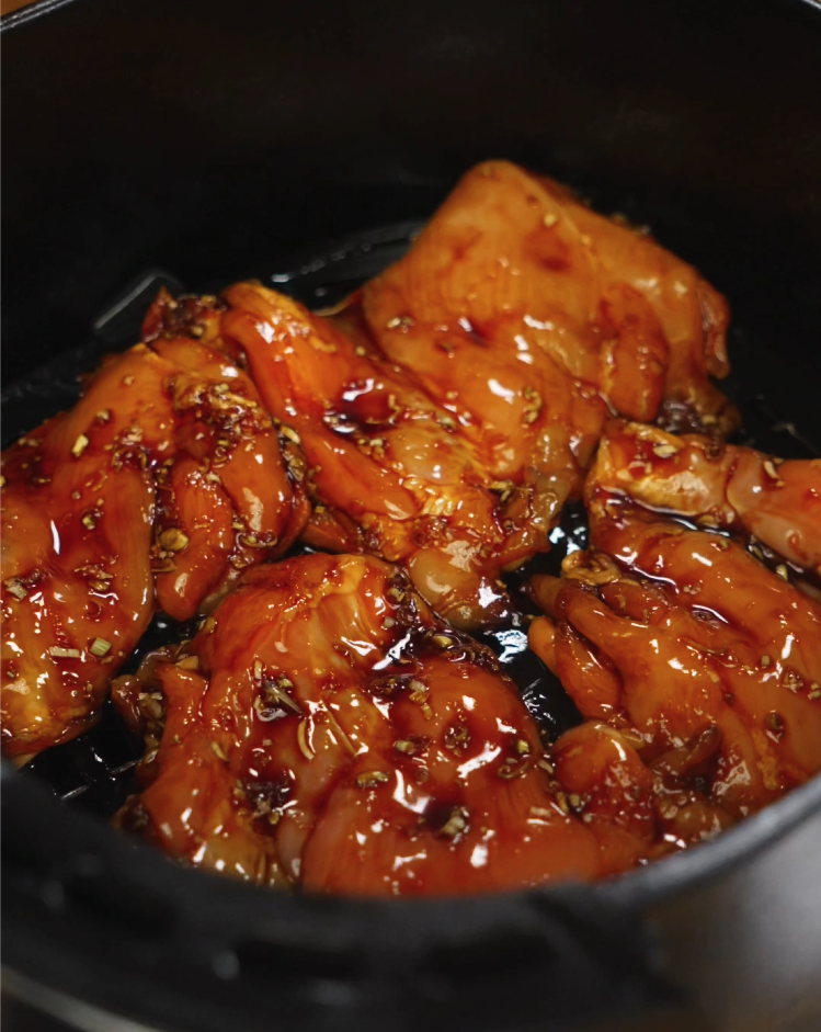 Marinated chicken thighs with lemongrass, garlic, and fish sauce placed in an air fryer basket, ready to be cooked.