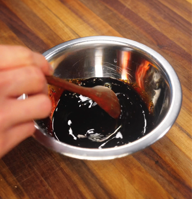 Stirring a glossy black pepper sauce mixture in a small stainless steel bowl, prepared as the main seasoning for the beef noodles.