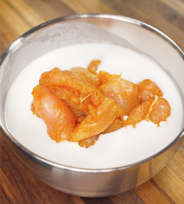 Seasoned chicken soaking in a bowl of buttermilk to tenderize before frying