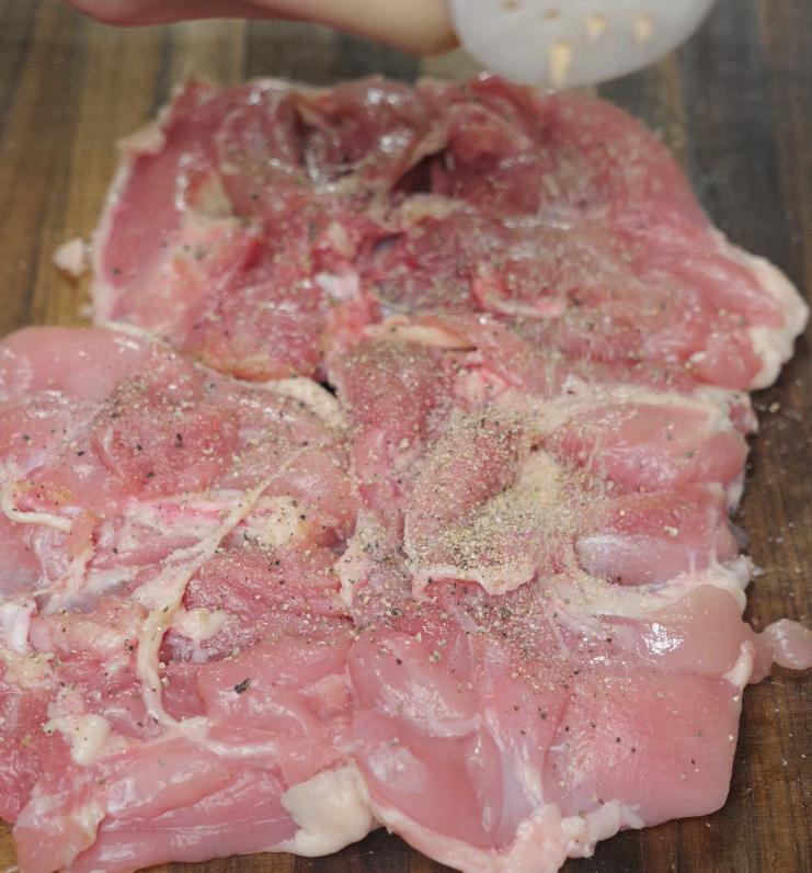 Raw chicken thighs are being seasoned with a sprinkle of salt, pepper, and garlic powder, prepping them for a flavorful sear in the Marry Me Chicken pasta recipe.