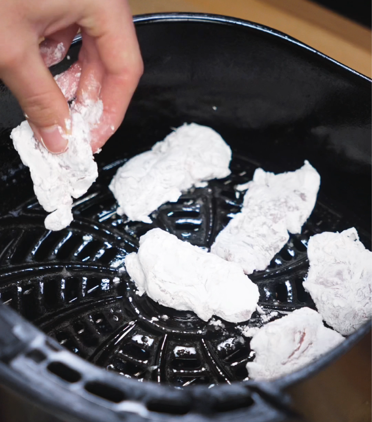 Hand placing cornstarch-coated chicken pieces into air fryer basket for crispy cooking