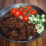 Plating beef tapa over a bed of rice with fresh cherry tomatoes and diced cucumbers for a colorful rice bowl.