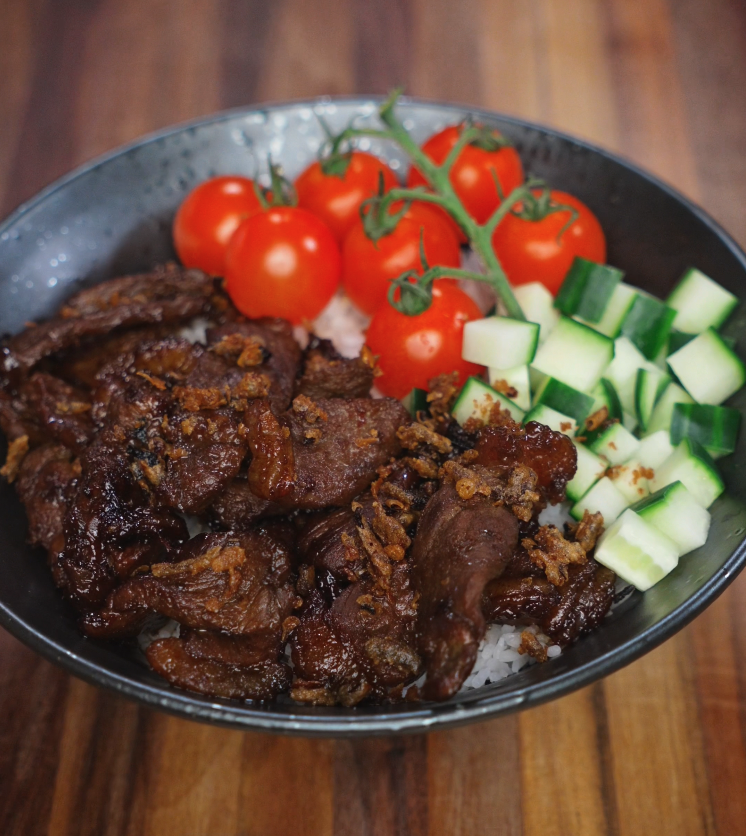 Plating beef tapa over a bed of rice with fresh cherry tomatoes and diced cucumbers for a colorful rice bowl.