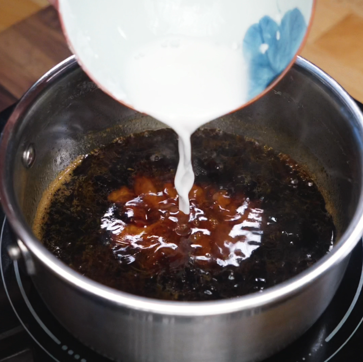 Cornstarch slurry being poured into pot of simmering teriyaki sauce to thicken