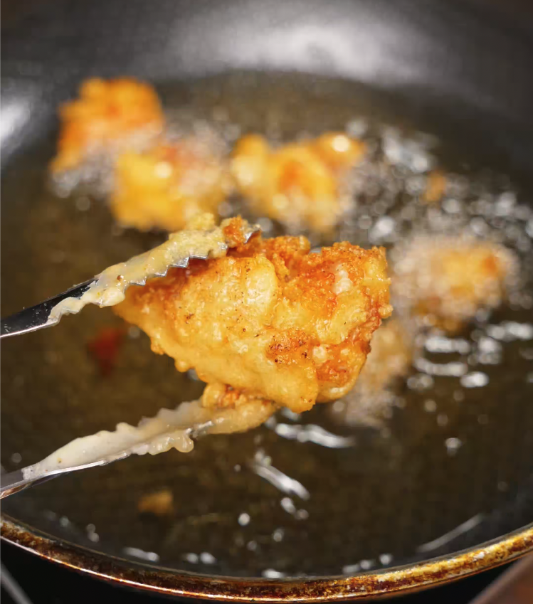 Tongs lifting crispy golden fried chicken out of hot oil during deep frying