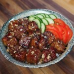 A beautifully plated bowl of shaking beef served over rice and garnished with fresh cucumber slices and tomato wedges for a vibrant, balanced presentation.