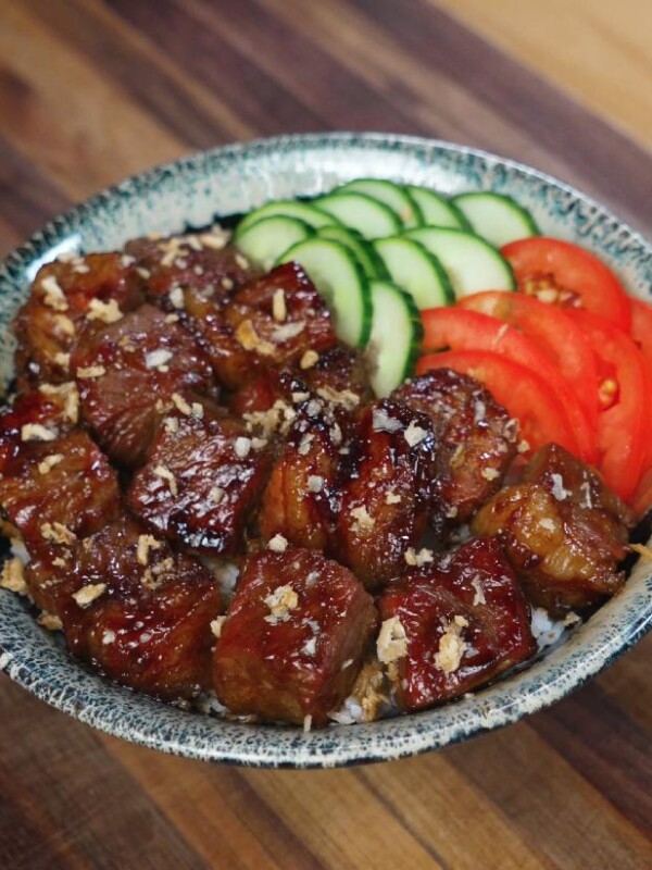 A beautifully plated bowl of shaking beef served over rice and garnished with fresh cucumber slices and tomato wedges for a vibrant, balanced presentation.