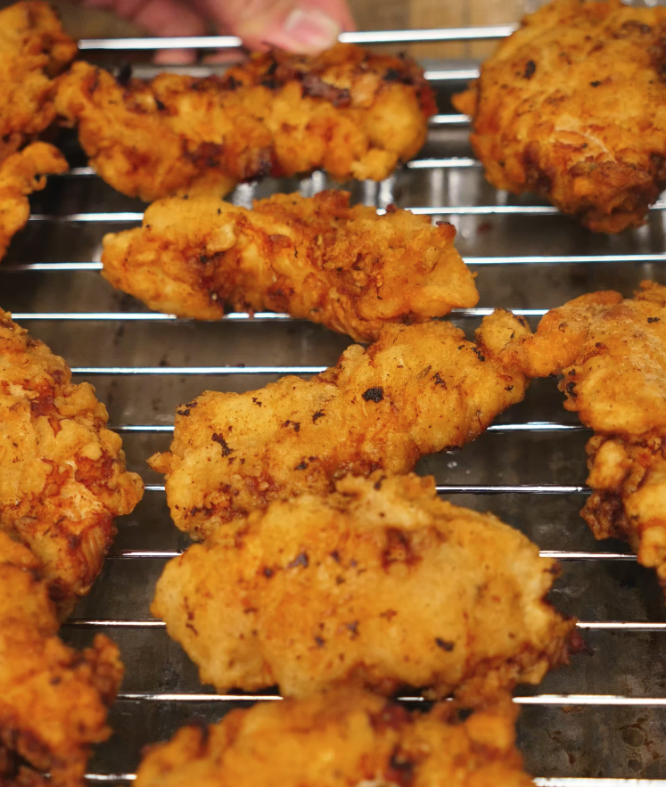 Golden-brown fried chicken tenders resting on a wire rack to keep them crispy while excess oil drains before saucing.