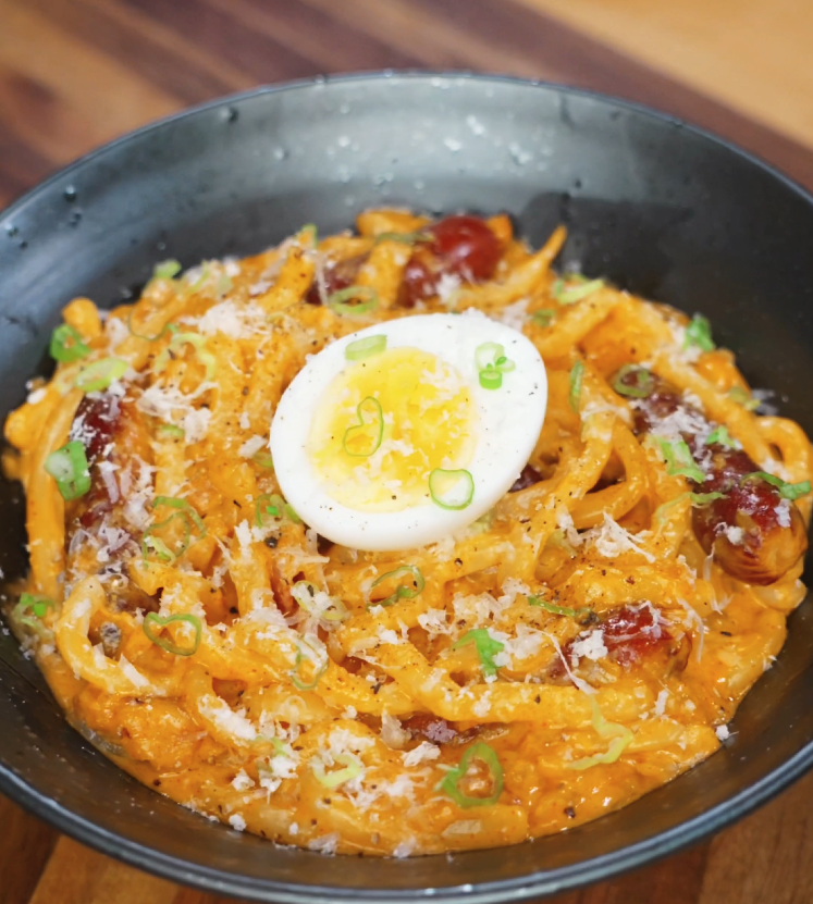 A bowl of rose noodles topped with grated cheese, chopped scallions, and a halved soft-boiled egg sits ready to serve, showcasing a rich and creamy texture.