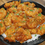 Plated sriracha honey butter chicken garnished with scallions and sesame seeds over white rice