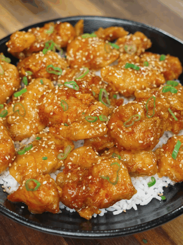 Plated sriracha honey butter chicken garnished with scallions and sesame seeds over white rice