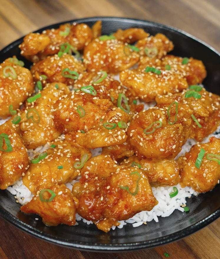 Plated sriracha honey butter chicken garnished with scallions and sesame seeds over white rice