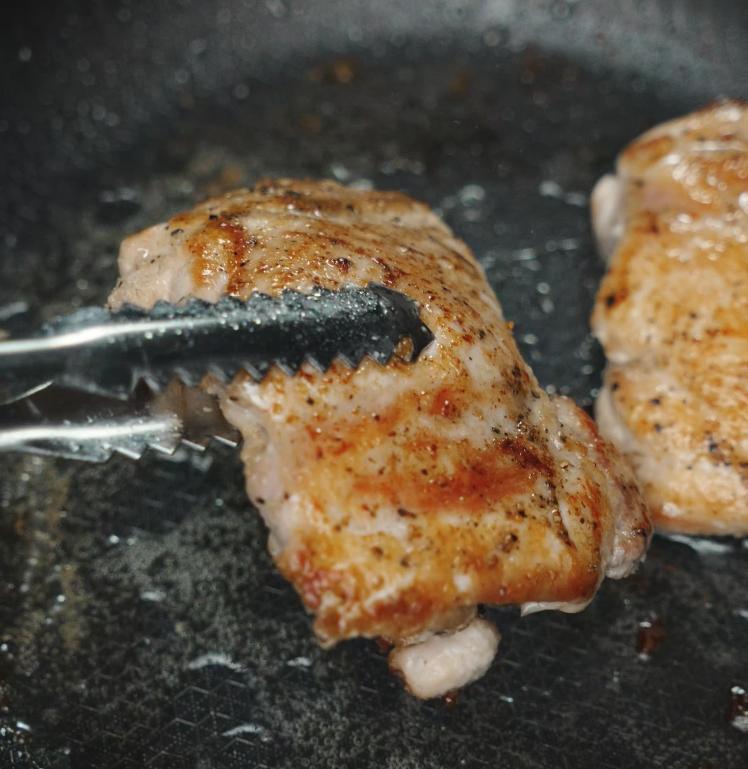 Chicken thighs are being flipped with tongs in a hot pan, showing off a beautifully golden brown sear, perfect for Marry Me Chicken pasta.