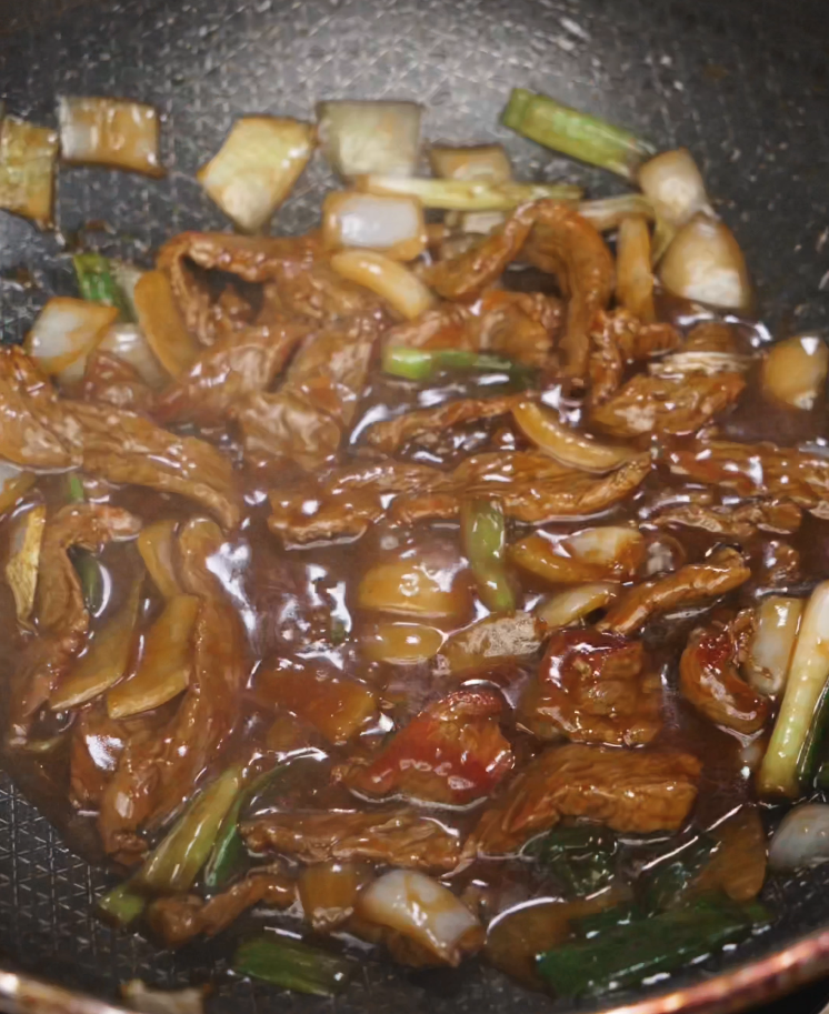 Simmering beef and onion stir fry in a bubbling glossy sauce until thickened and well coated, with onions and scallions throughout.