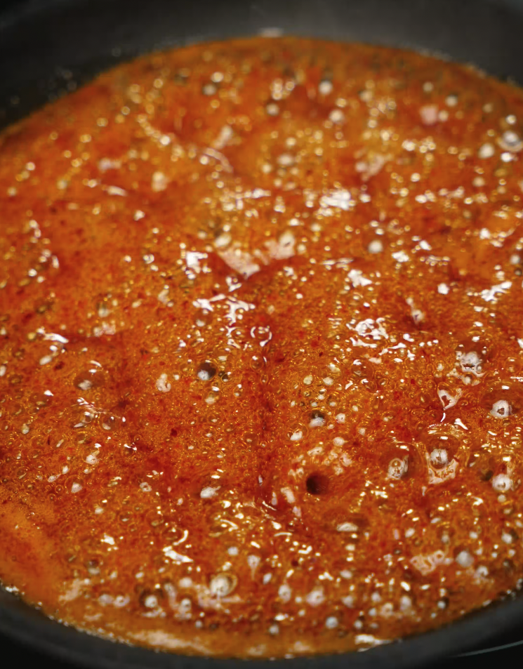 Bubbling hot honey glaze cooking down in a pan, rich with chili flakes and spices, ready to coat the crispy fried tenders.