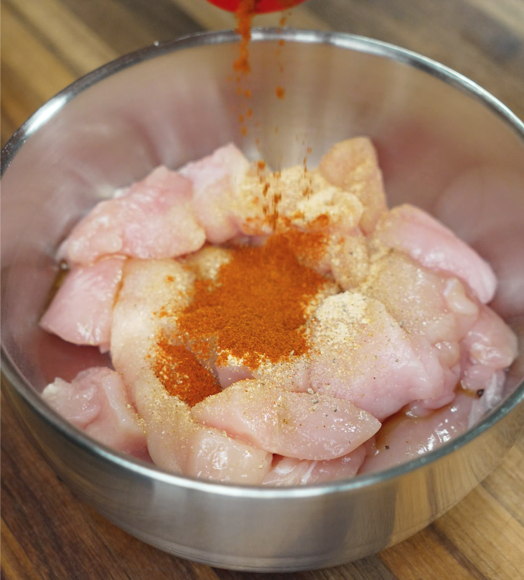 Raw chicken in a metal bowl being seasoned with spices for sriracha honey butter fried chicken