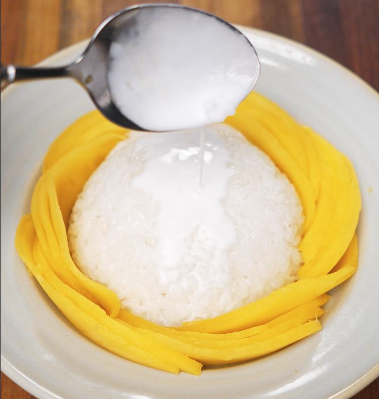 Spoon drizzling thick coconut cream over the top of the plated mango sticky rice for extra richness.